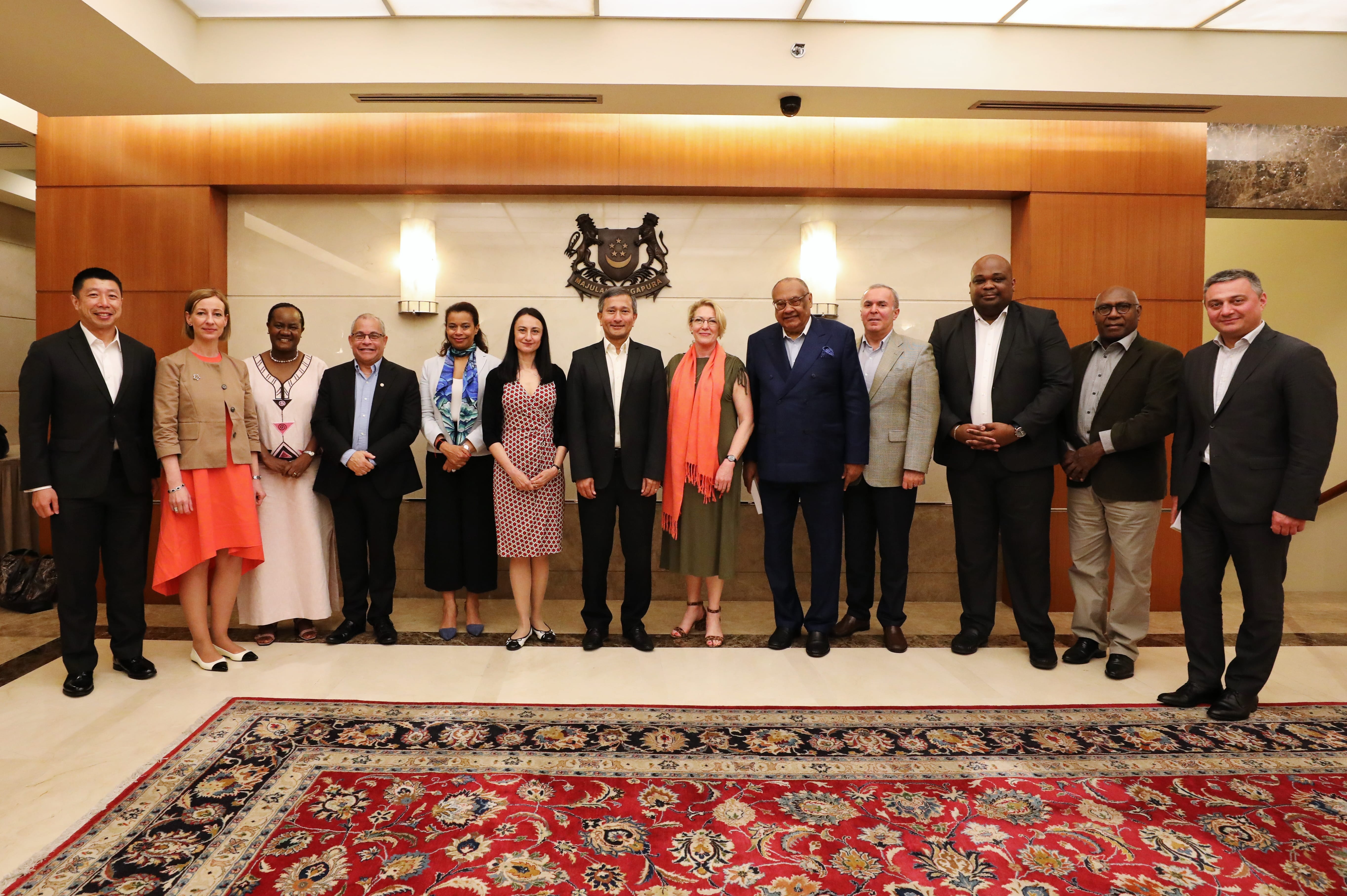 Group of people posing in formal wear in front of a wooden wall with the Singapore coat-of-arms.